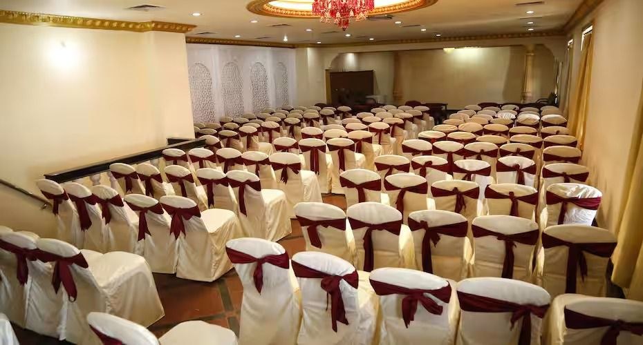 Banquet hall set in rows with cream chair covers and maroon bows under a red chandelier