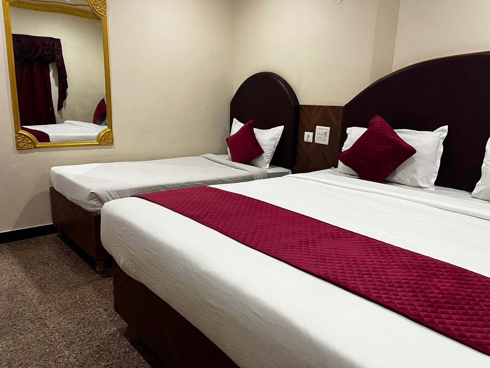 Twin room with maroon bed runners, round headboards and a gold-framed mirror