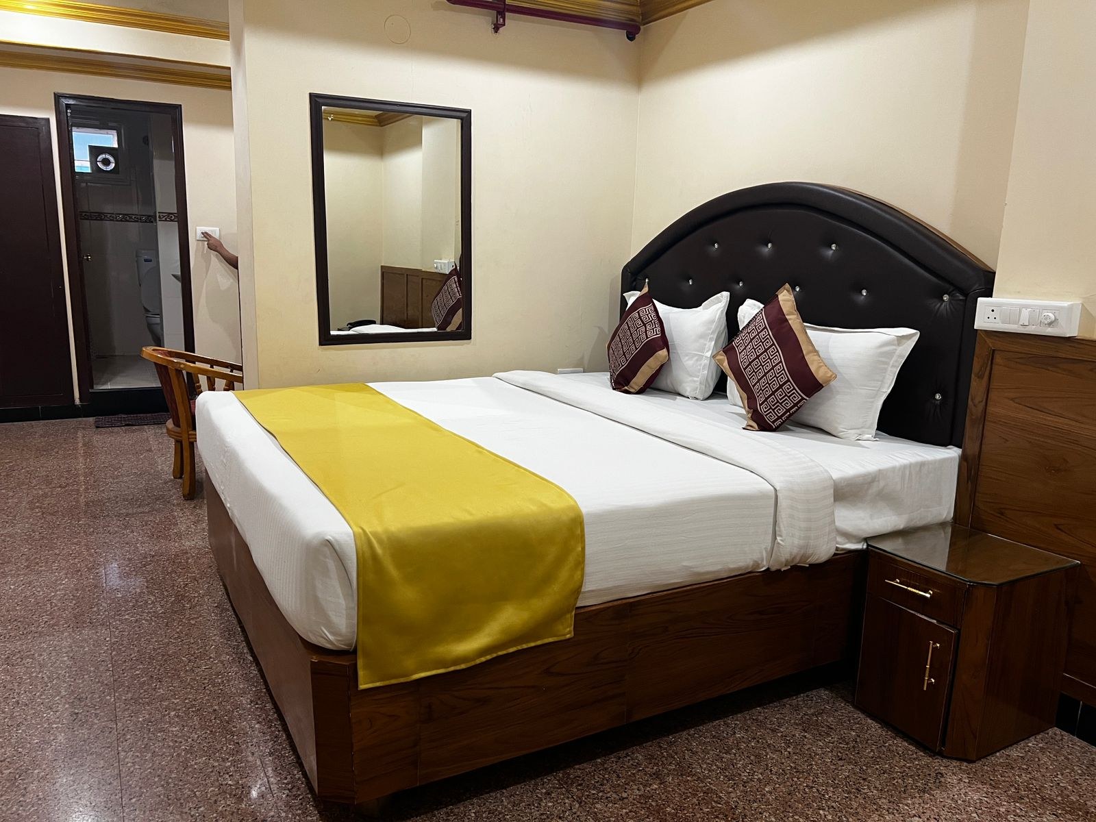 Spacious suite with a yellow bed runner, tufted headboard and attached bathroom